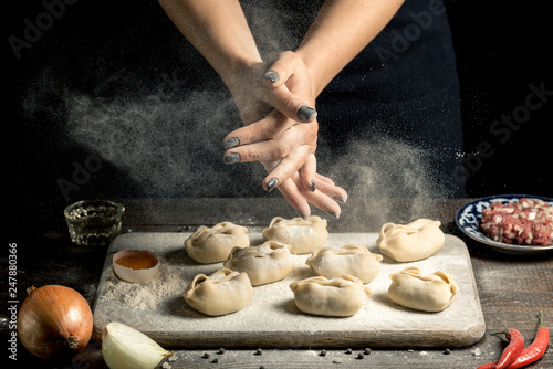 Uzbek national food manta, like dumplings, on a wooden board, lie in flour with an egg. Hands in flour clap