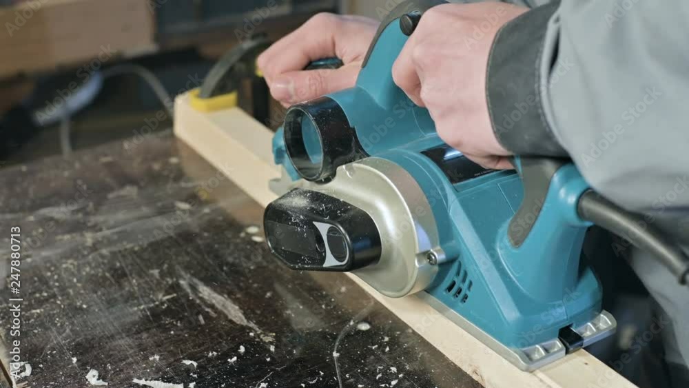 Close-up of a carpenter's hand working with an electric plane in a home workshop. Finishing wooden parts Close-up of a carpenter's hand working with an electric plane in a home workshop. Finishing wooden parts