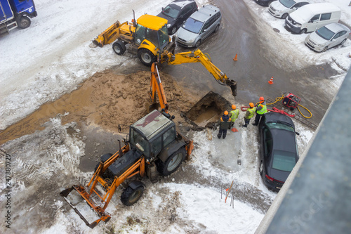 A group of road workers from public utilities in reflective special vests are discussing an emergency when digging a hole to eliminate the leakage of pipes in the middle of winter