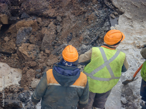 A group of road workers from public utilities in reflective special vests are discussing an emergency when digging a hole to eliminate the leakage of pipes in the middle of winter