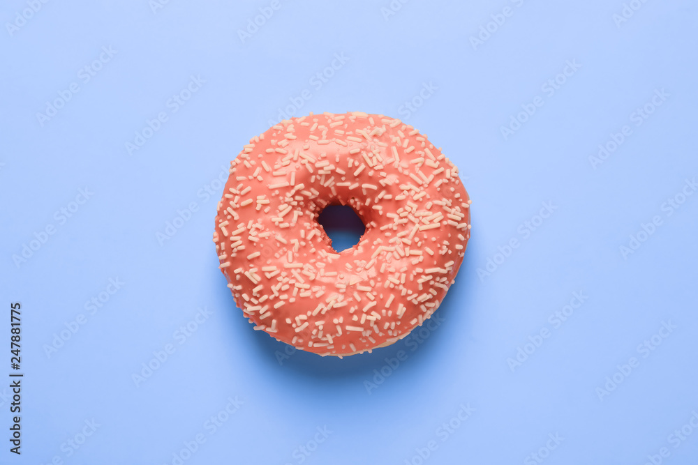 Delicious doughnut with orange glaze and sprinkles on blue background, top view