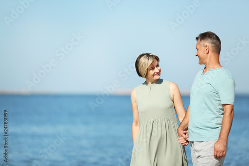 Happy mature couple holding hands at beach on sunny day