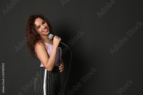Curly African-American woman in stylish clothes posing with microphone on black background. Space for text