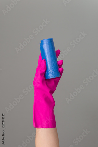 Hand in rubber glove holds colored garbage bag on neutral background. The concept of bright spring, spring cleaning.