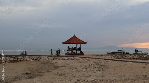 Tourists on vacation relaxing along the shores of Sanur Beach, Bali, Indonesia. Tourists are walking along the paths and relaxing under a beautiful pagota photo