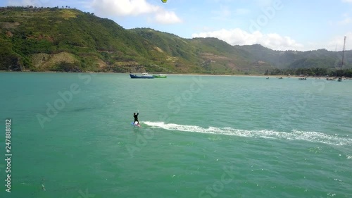 Tracking shot of a kiteboarder moving his kite vigorously with fishing boats in the background. Aerial footage captured in Kuta, Lombok, Indonesia.