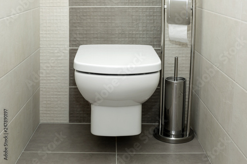 White toilet bowl in modern bathroom with paper holder and toilet brush.