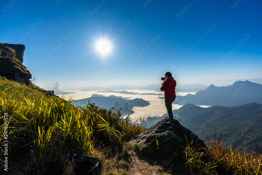 Photographer hand holding camera and standing on top of the rock in nature. Travel concept.