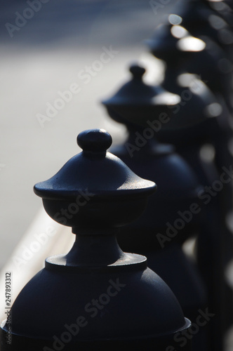 A long row of black decorative piece that serves as fence and backing for a long bench in a park.