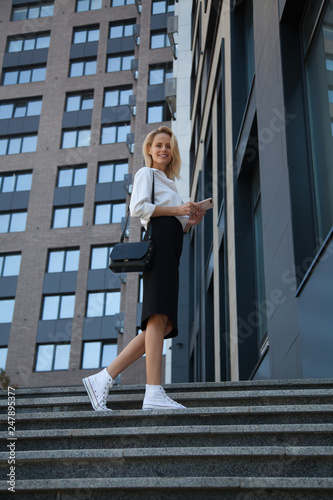 Smiling business woman with bag and cell phone against office building