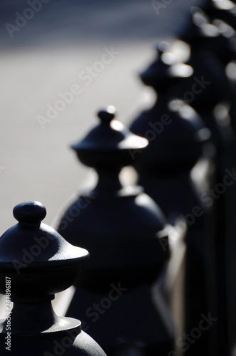 A long row of black decorative piece that serves as fence and backing for a long bench in a park.