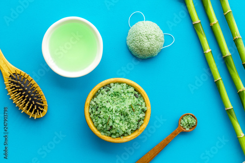 Asian spa treatment concept with natural ingredients. Spa salt, lotion, sponge near bamboo on blue background top view