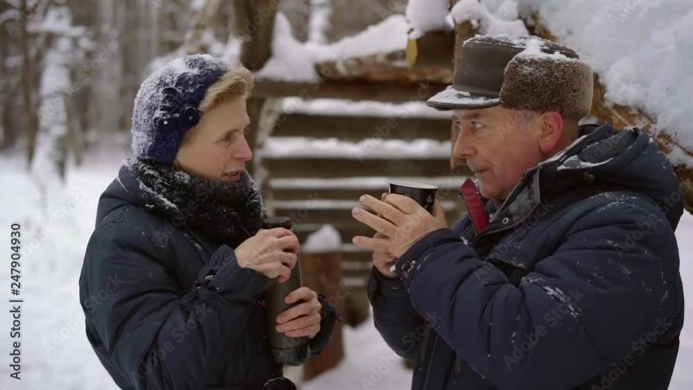 old man is drinking hot tea and talking with his wife holding thermos bottle, standing outdoors