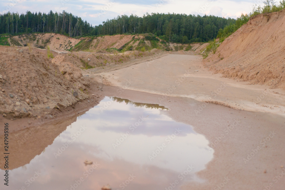 a long road of rubble with puddles along the quarry and forest