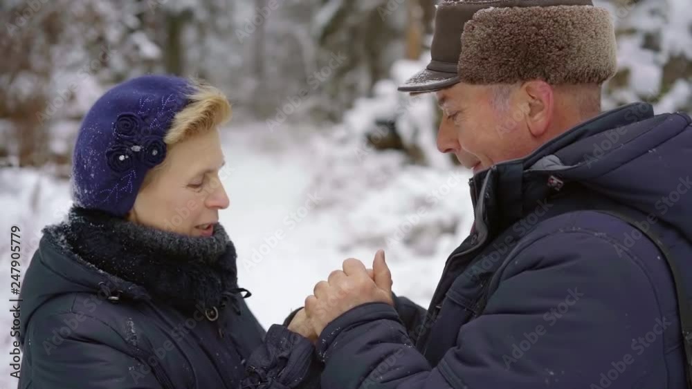 elderly man is warming hands of his beloved wife, stroking them, standing outdoors in cold winter day elderly man is warming hands of his beloved wife, stroking them, standing outdoors in cold winter day