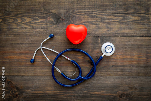 Heart health, health care concept. Stethoscope near rubber heart on dark wooden background top view copy space