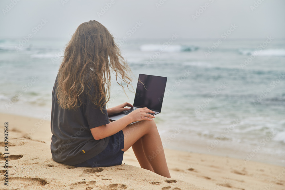 Young girl working at the computer on the beach. The freelancer working on the beach.