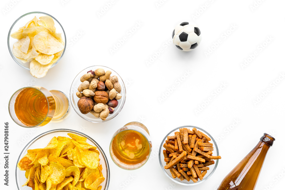 Snacks for watching football on TV. Watching sports. Chips, nuts, rusks near beer and soccer ball on white background top view copy space Snacks for watching football on TV. Watching sports. Chips, nuts, rusks near beer and soccer ball on white background top view copy space
