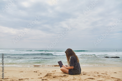 Young girl working at the computer on the beach. The freelancer working on the beach.