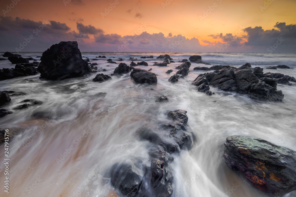 A scenery of sunrise with amazing unique rock formation and beautiful  flow of wave at Kemasik beach, Terangganu Malaysia. Soft focus during long exposure shot.