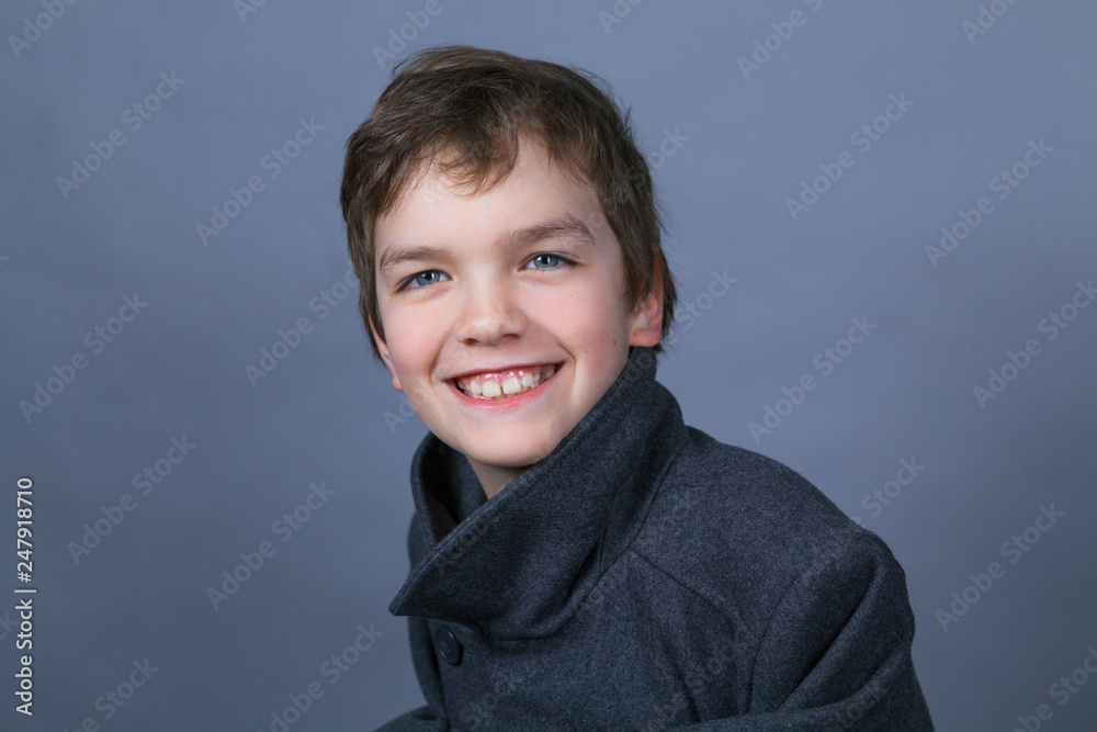 Portrait of a handsome boy in a black coat on a gray background
