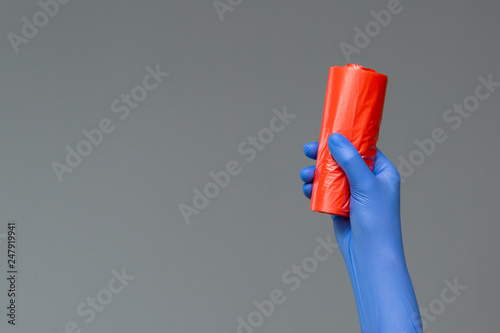 Hand in rubber glove holds colored garbage bag on neutral background. The concept of bright spring, spring cleaning.
