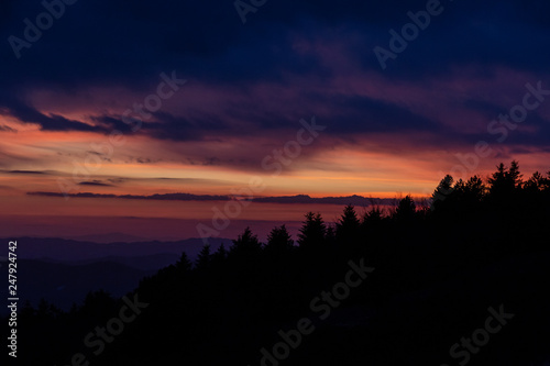 Trees silhouettes against a beautifully colored sky at dusk  with mountains layers in the background