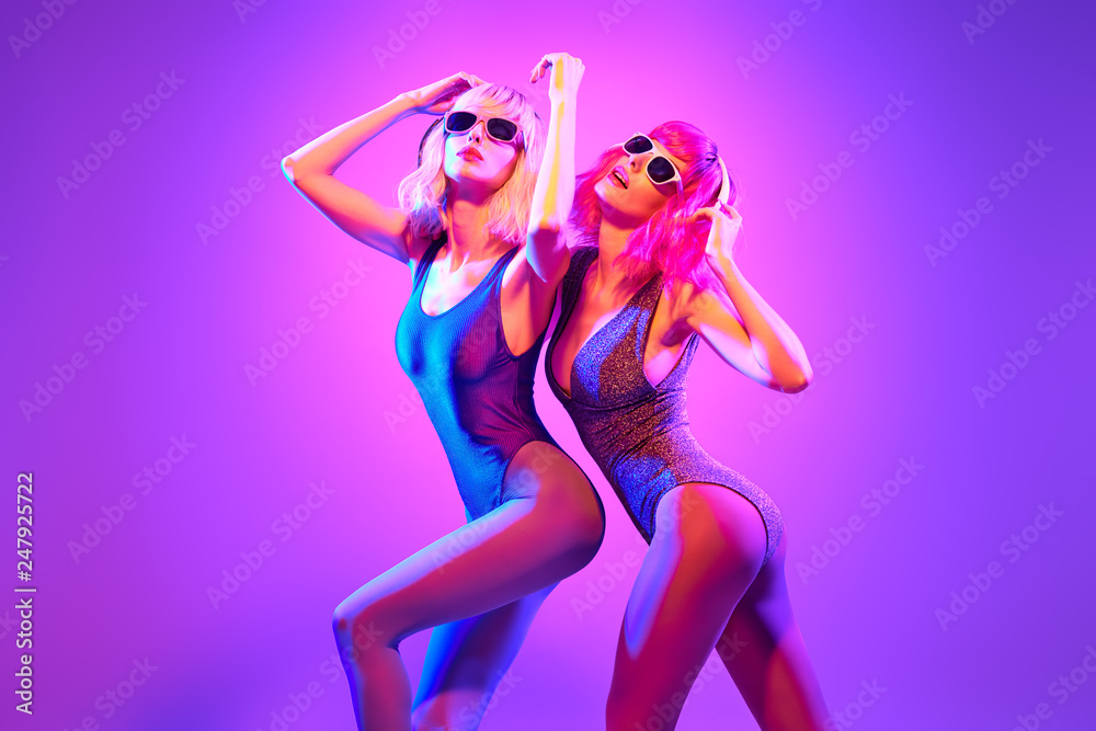 Two sexy fashionable DJ girl in party outfit dance. Colorful neon uv light. Rave house music vibes. Model woman with Dyed Hair, makeup. High Fashion. Night Club neon concept.