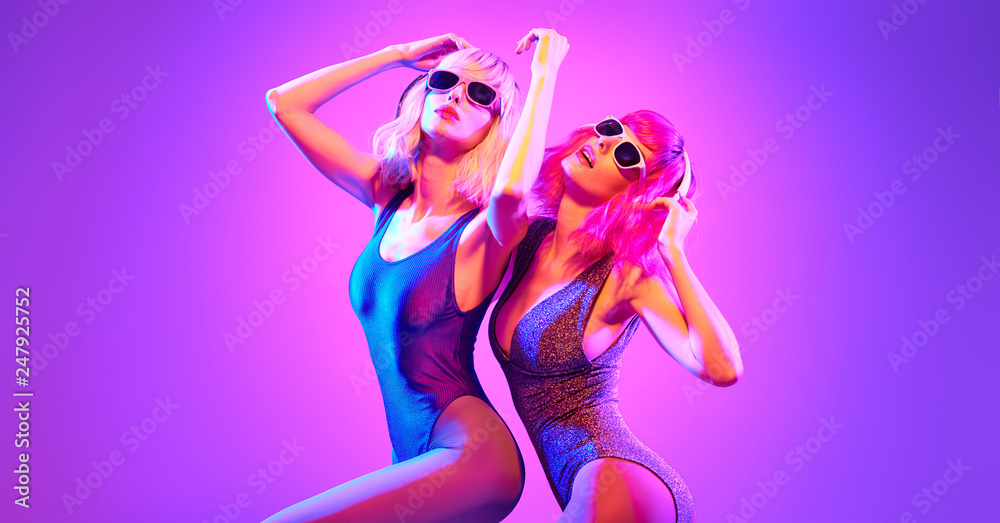 Fashion. Two sexy DJ girl in Colorful neon light dance. Glamour party fitness woman with Dyed Hair in Trendy headphones. Young beautiful model enjoy nightlife. Creative art banner Fashion. Two sexy DJ girl in Colorful neon light dance. Glamour party fitness woman with Dyed Hair in Trendy headphones. Young beautiful model enjoy nightlife. Creative art banner