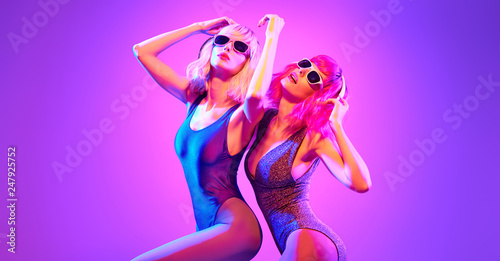 Fashion. Two sexy DJ girl in Colorful neon light dance. Glamour party fitness woman with Dyed Hair in Trendy headphones. Young beautiful model enjoy nightlife. Creative art banner