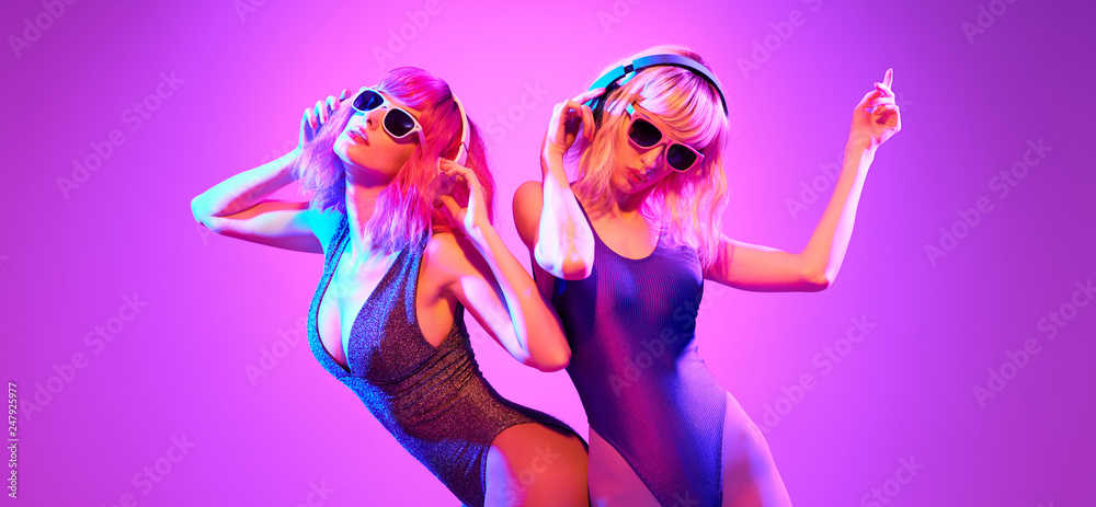 Fashion. Two DJ girl with Dyed Hair, party makeup in Colorful neon light enjoy music, friends. Disco 80s 90s vibes. Model woman in fashionable bodysuit, make up dancing. Art uv neon banner