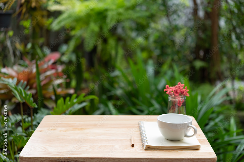 Coffee cup notebook,brown pencil and beautiful red dried flower in glass vase on wood table with fresh green garden background,outdoor workspace Coffee cup notebook,brown pencil and beautiful red dried flower in glass vase on wood table with fresh green garden background,outdoor workspace