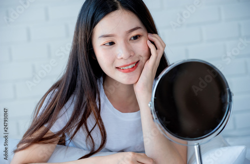 Asian teenage woman looking at mirror and squeeze acne problem on her face, skin care concept.