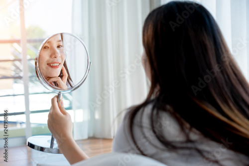 Asian teenage woman  looking at mirror and squeeze acne problem on her face  skin care concept.