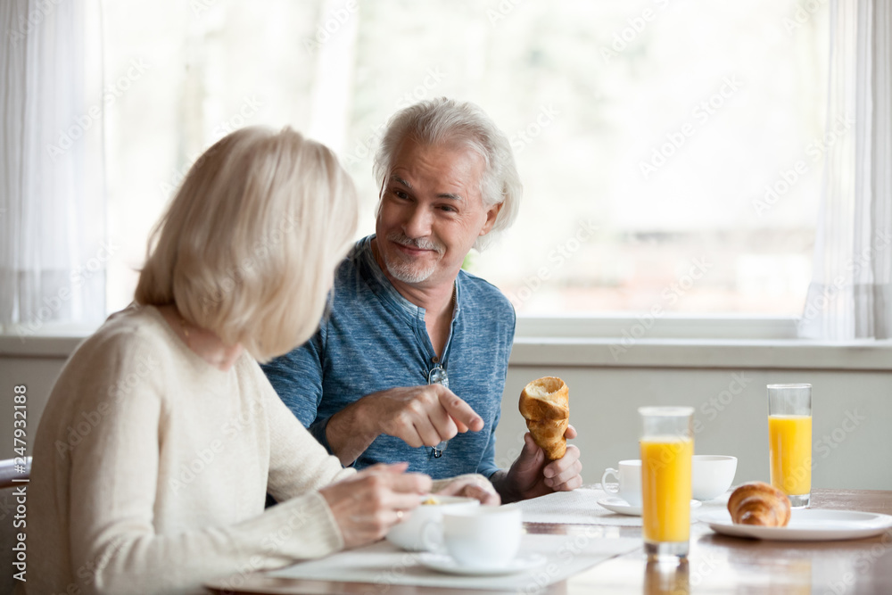 Positive aged spouses eating breakfast talking sitting in the kitchen Positive aged spouses eating breakfast talking sitting in the kitchen