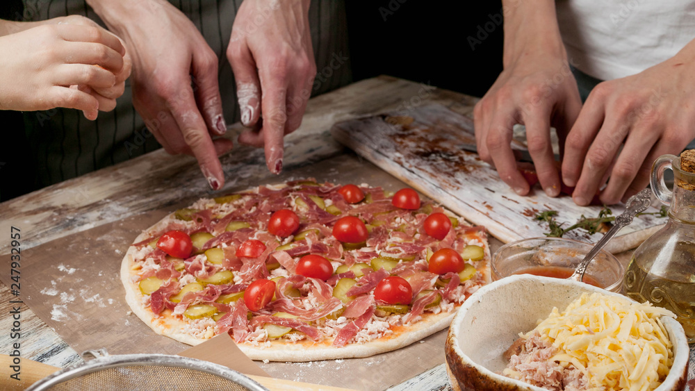 Horizontal Food Banner. Mom and her children prepare delicious homemade pizza with prosciutto and vegetables in the kitchen. Hands of people close up