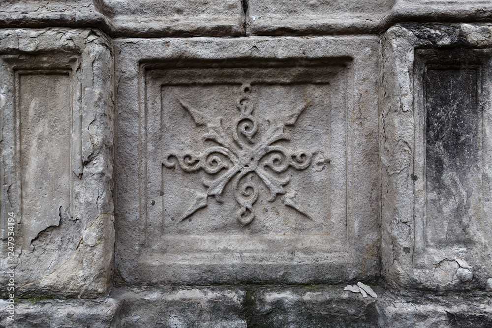 Close-up: a stone element of an old ornament on a crumbling wall with cracks in an ancient temple
