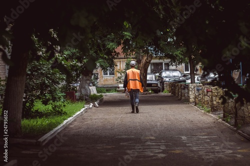 Wallpaper Mural a janitor or a territory cleaner in special clothes walks between the trees in the courtyard of residential buildings; summer time; representative of the municipal service in an orange vest Torontodigital.ca