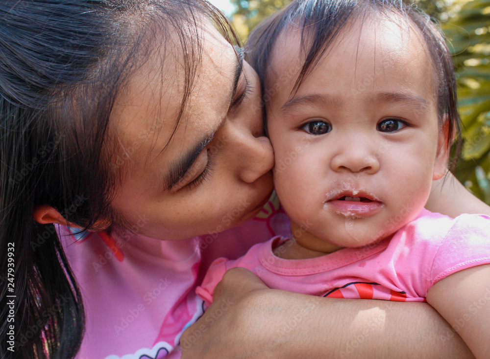 Asian mom and Daughter walk in the park, mom kisses a little girl on the cheek. Asian mom and Daughter walk in the park, mom kisses a little girl on the cheek.