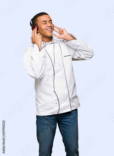 Young afro american chef man listening to music with headphones on isolated background