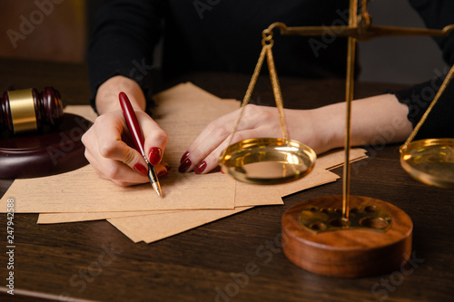 Foto Young lawyer woman with bright red maniqure sitting at table and writing somethi