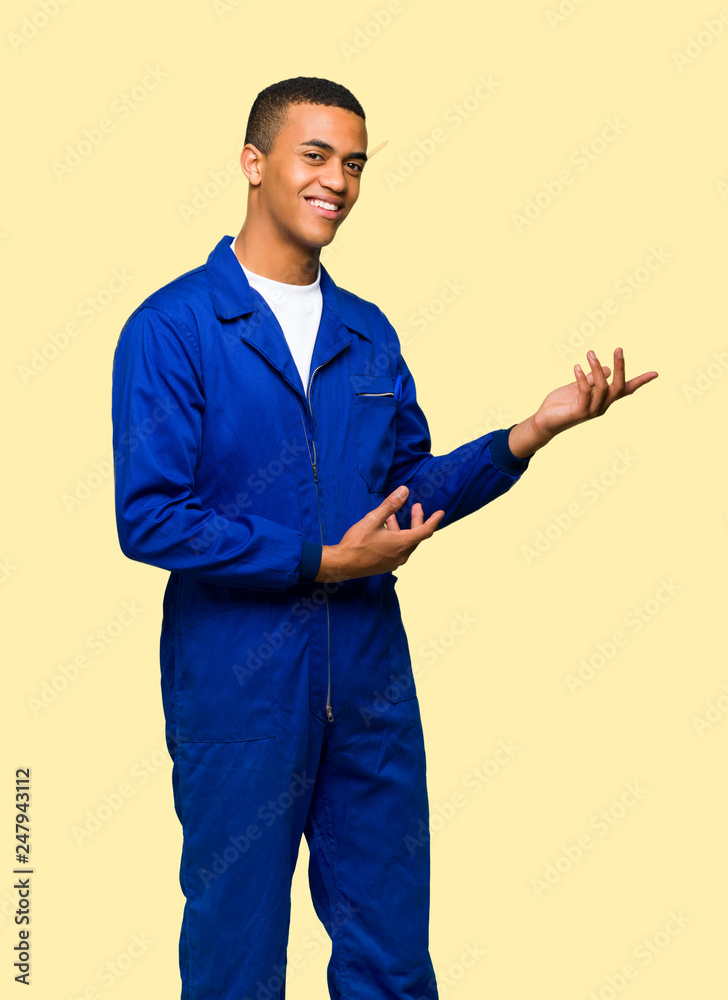 Young afro american worker man extending hands to the side for inviting to come on isolated background Young afro american worker man extending hands to the side for inviting to come on isolated background