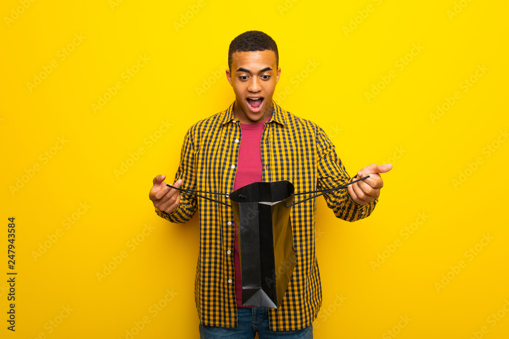 Young afro american man on yellow background surprised while holding a lot of shopping bags Young afro american man on yellow background surprised while holding a lot of shopping bags