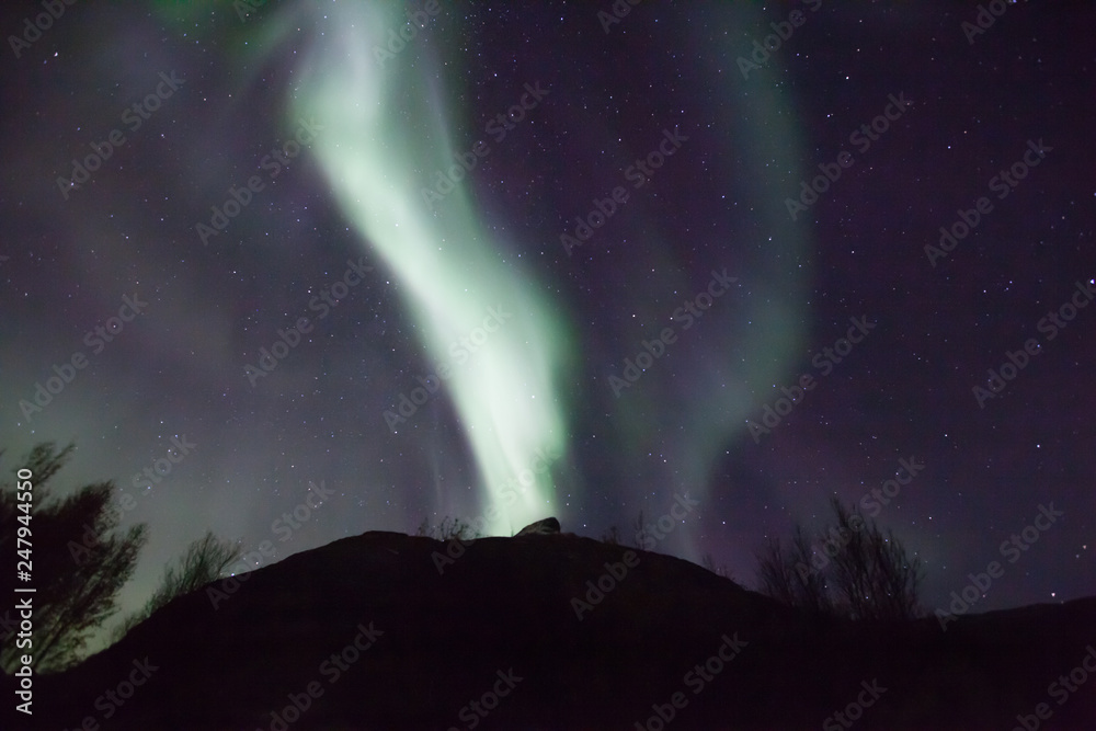 northern lights in Norway in green, blue and violet colours and a silhouette  of a mountains in front