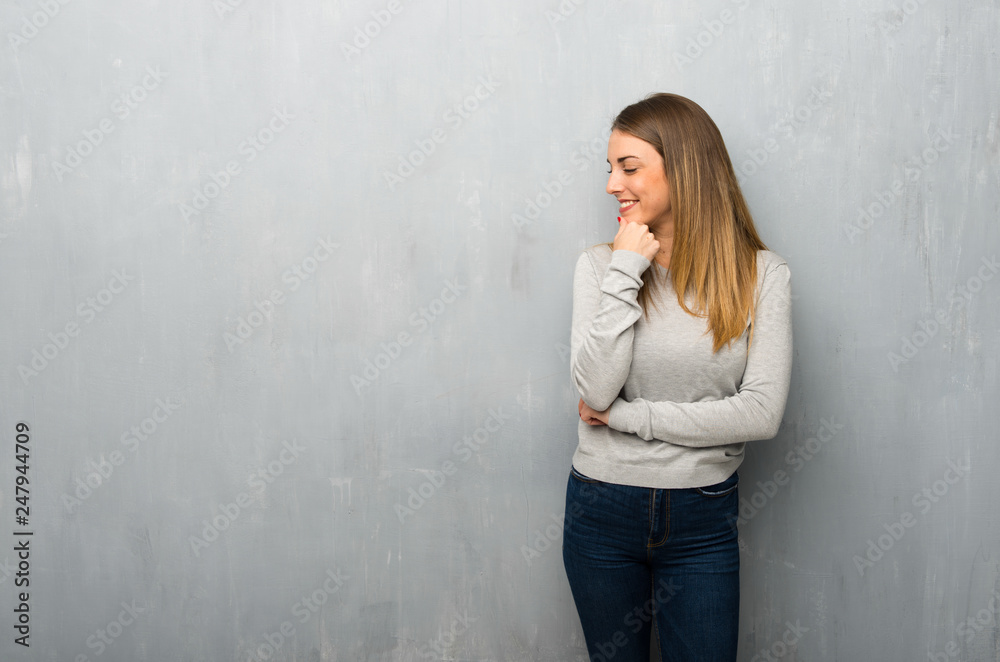 Young woman on textured wall looking to the side with the hand on the chin Young woman on textured wall looking to the side with the hand on the chin