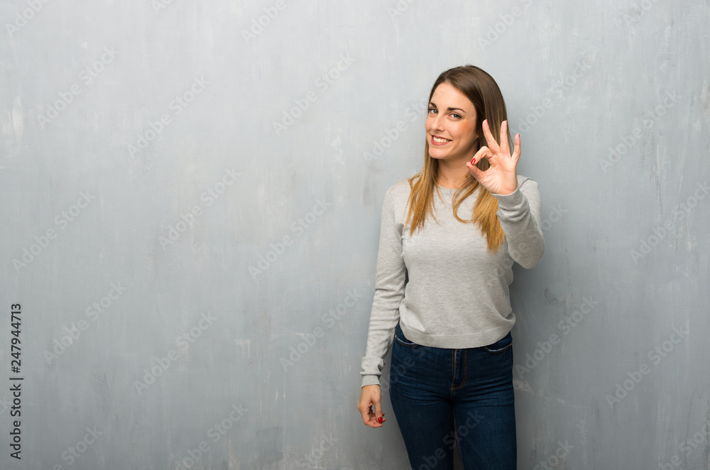 Young woman on textured wall showing an ok sign with fingers Young woman on textured wall showing an ok sign with fingers