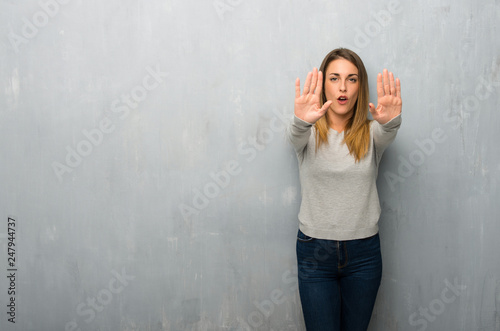 Young woman on textured wall making stop gesture for disappointed with an opinion