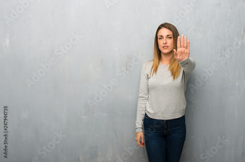Young woman on textured wall making stop gesture denying a situation that thinks wrong