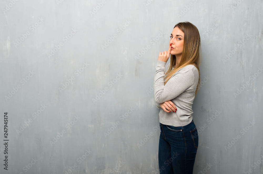 Young woman on textured wall showing a sign of closing mouth and silence gesture Young woman on textured wall showing a sign of closing mouth and silence gesture
