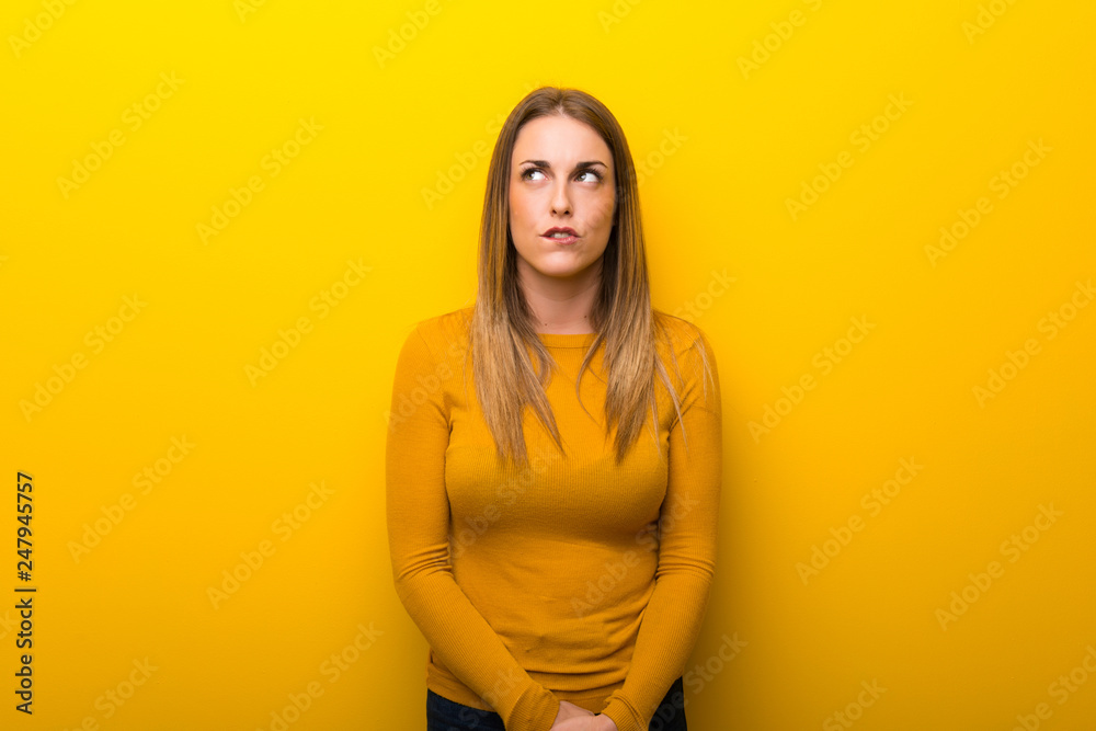 Obraz premium Young woman on yellow background with confuse face expression while bites lip